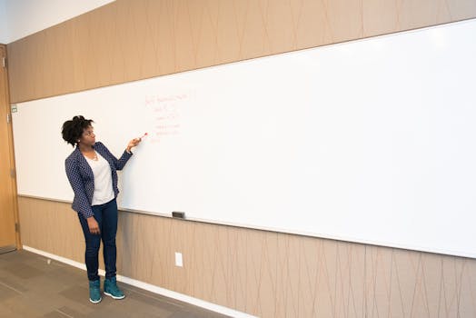 Black female educator explaining concepts on whiteboard in conference room setting.