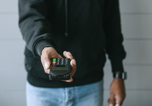 Hand offering a wireless payment terminal for transactions. Modern cashless payment technology.