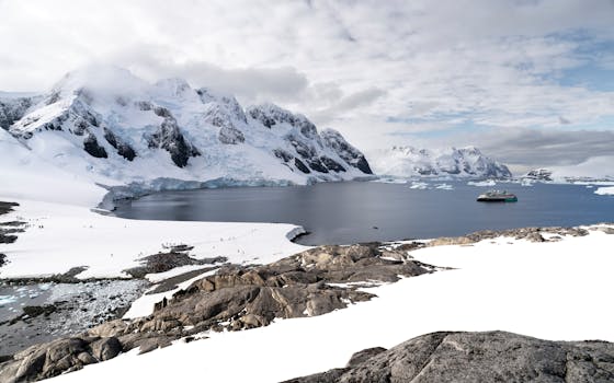 Scenic Antarctic view with icy mountains, calm waters, and a solitary boat.