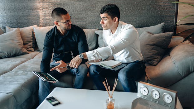 Two men discussing business ideas on a sofa using a tablet in a cozy home office setting.