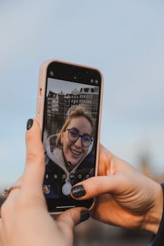 Close-up of a woman taking a selfie outdoors with a smartphone, smiling happily.