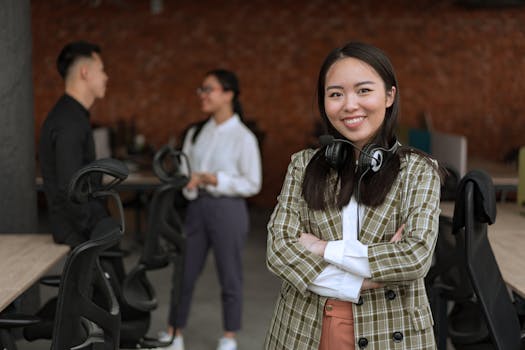 Confident Asian woman with headset and crossed arms in a modern office setting.